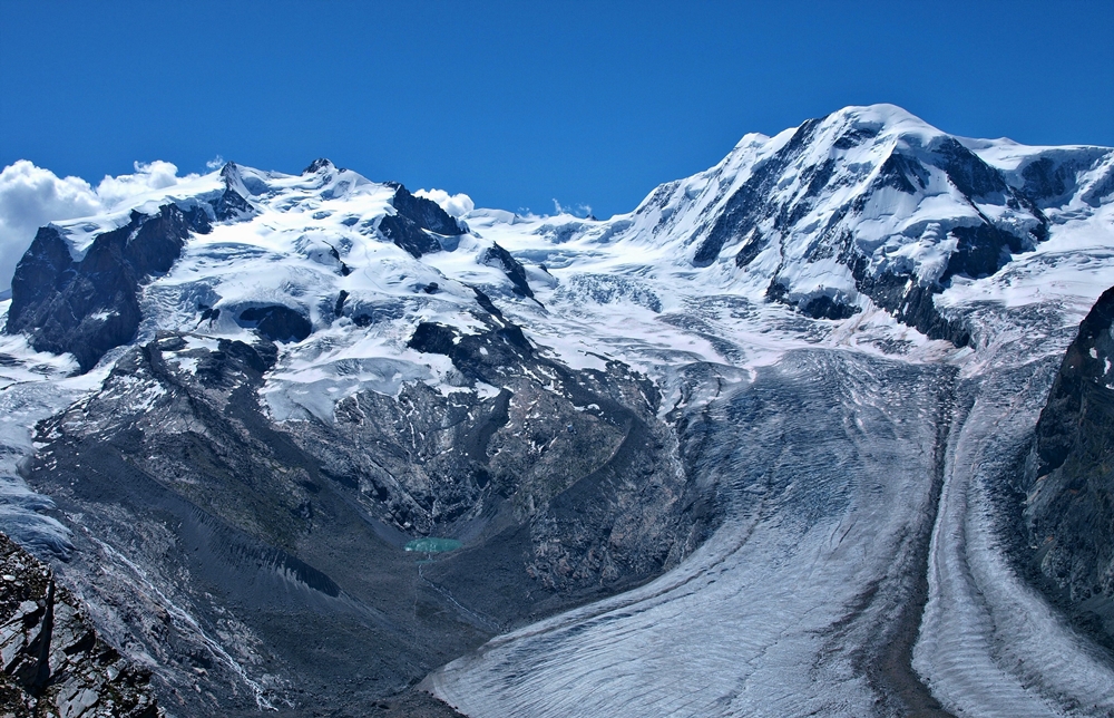 Vpravo: Dufourspitze, najvyššia hora Švajčiarska a druhá najvyššia hora Álp. Vľavo Liskamm, štvrtá najvyššia hora Álp. Medzi nimi vidieť začiatok druhého najväčšieho ľadovcového systému v Alpách – Gornerský ľadovec. Fotené začiatkom leta, keď sa snehy na vrcholkoch hôr topia.